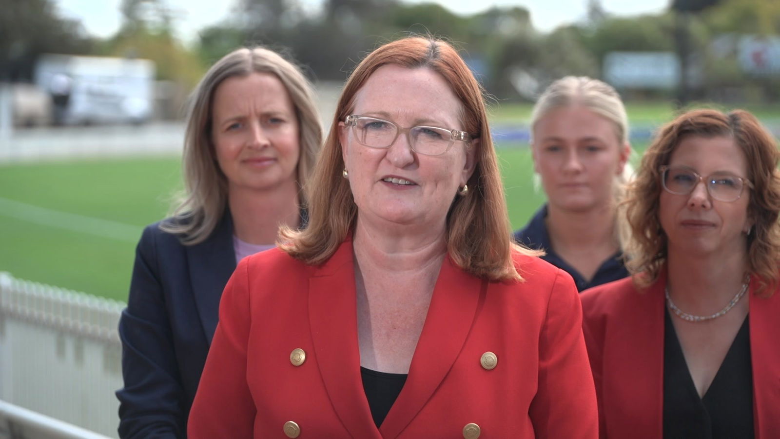 Four women in black and red stand facing the camera in front of a sports field.