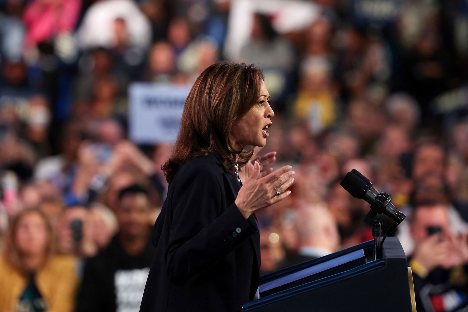 A side profile shot of Kamala Harris raising her hands during her speech at a rally