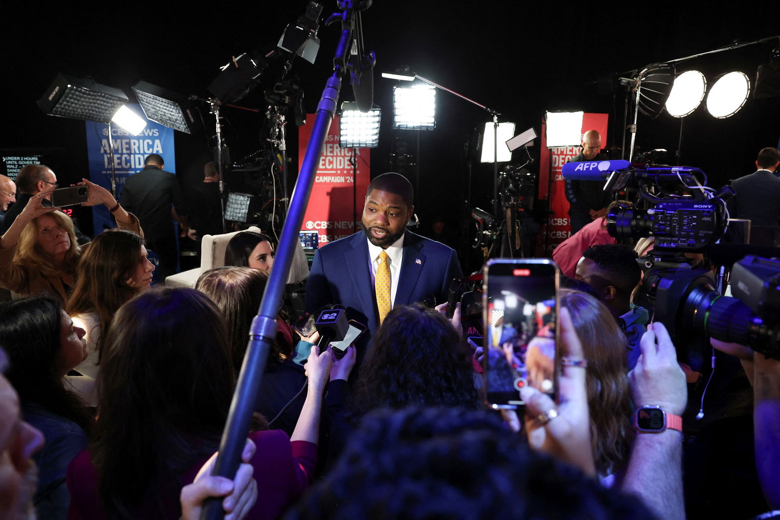 Donalds stands under light stands, surrounded by journalists