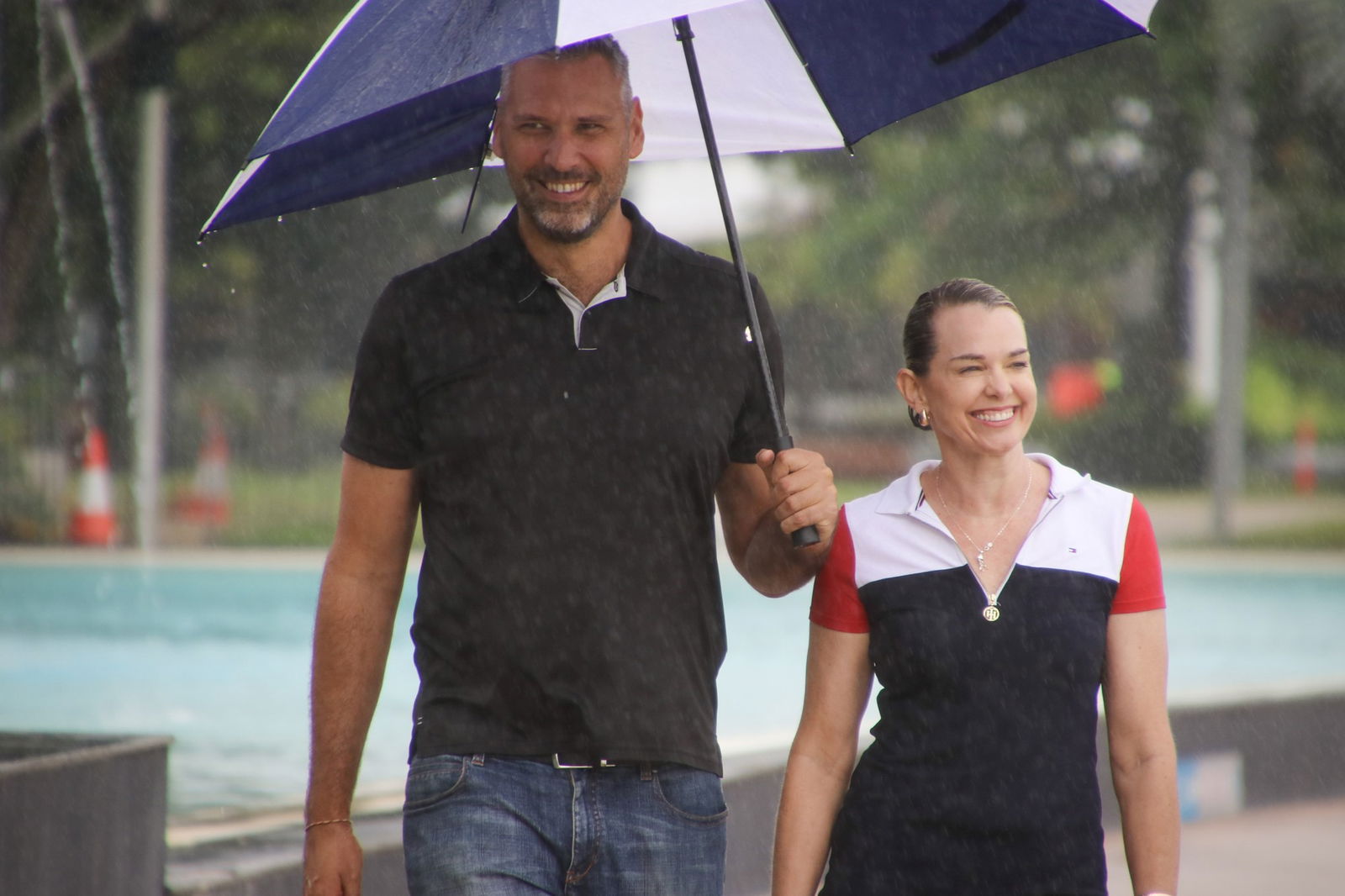 A man holds a blue and white umbrella and stands next to a smiling woman