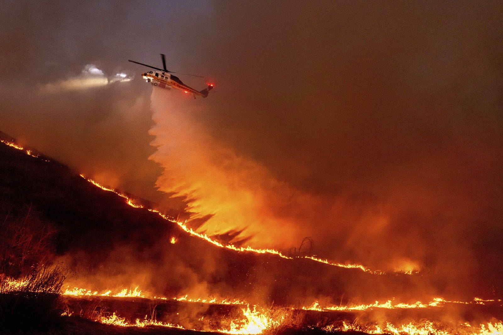 A helicopter dropping water onto a fire at night