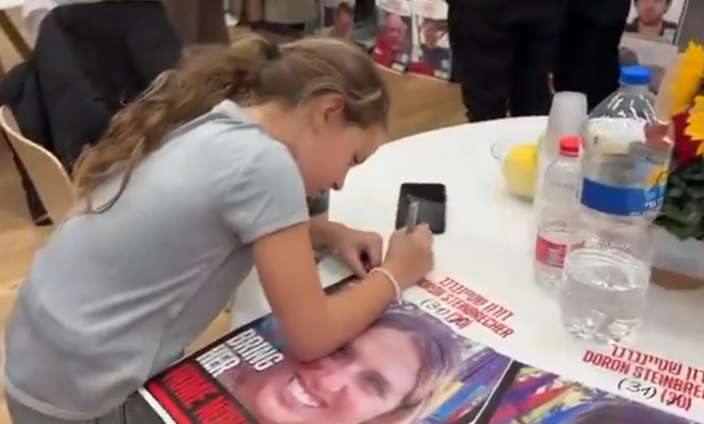 A young girl writes on a poster featuring the face of a young woman.