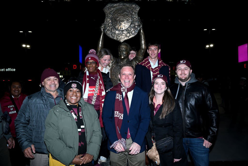 Queensland Premier Steven MIles smiles maniacally with a group of people in front of a statue of Wally Lewis.