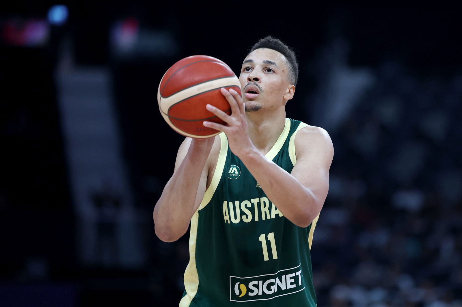 Dante Exum, wearing an Australian team uniform, holds a basketball with a focussed expression on a basketball court