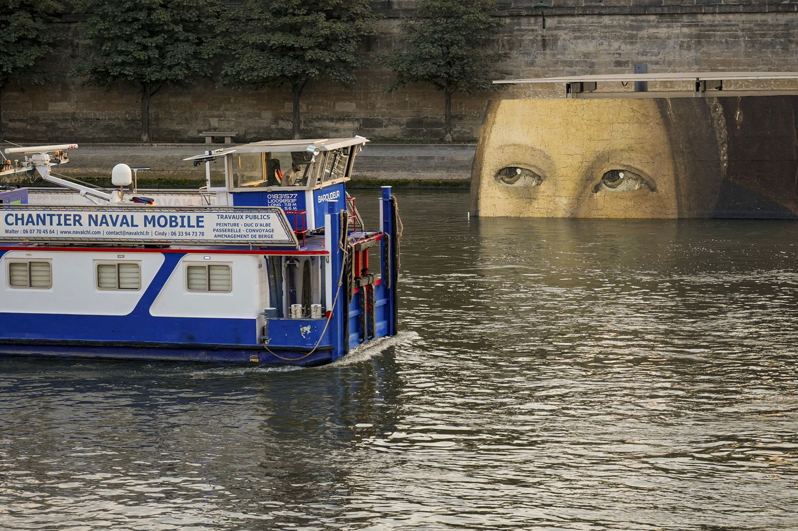 A painting in the background appears to look at a tugboat on the River Seine hauling away parts of the start of the postponed men's triathlon at the Paris Olympics.