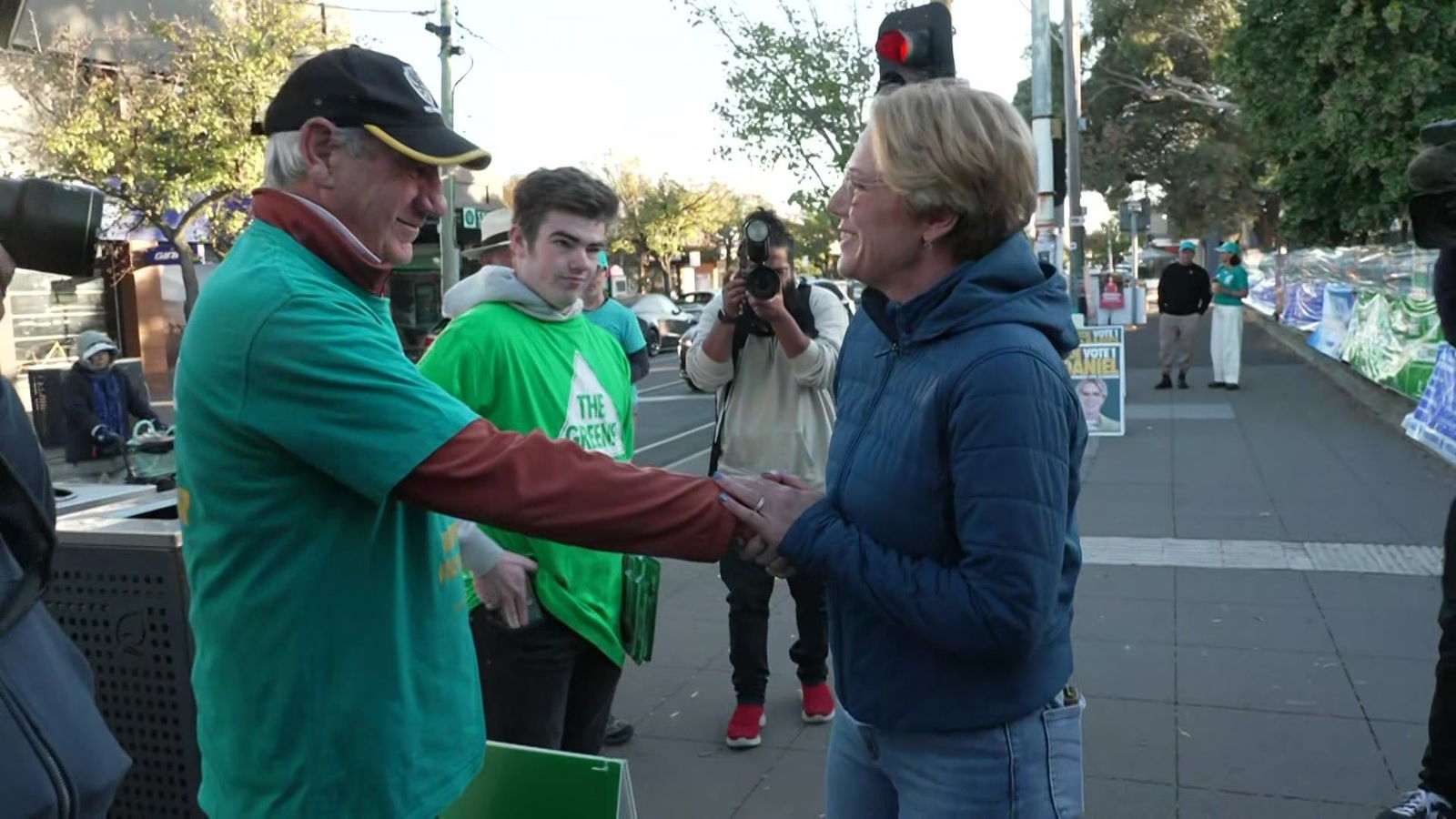 Zoe Daniels wearing a puffer jacket and shaking the hand of a man wearing a green t-shirt
