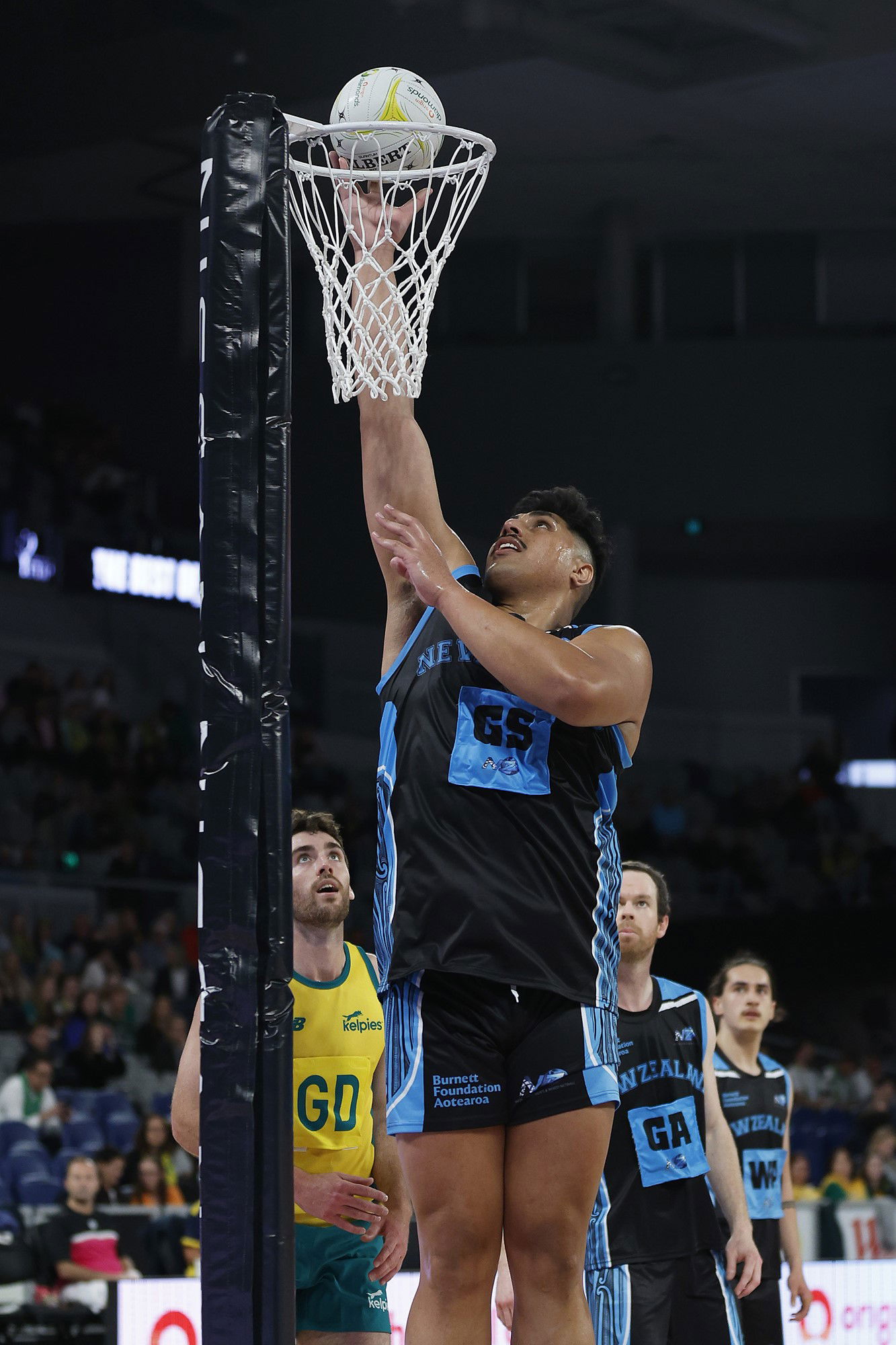 A male netballer jumps high and puts the ball through the net