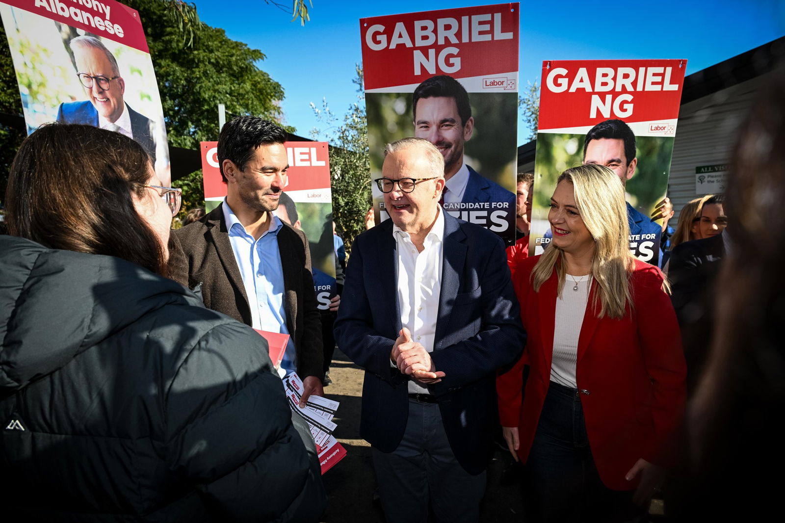 Anthony Albanese, Gabriel Ng and Jodie Haydon standing together speaking to a woman in a black puffer jacket