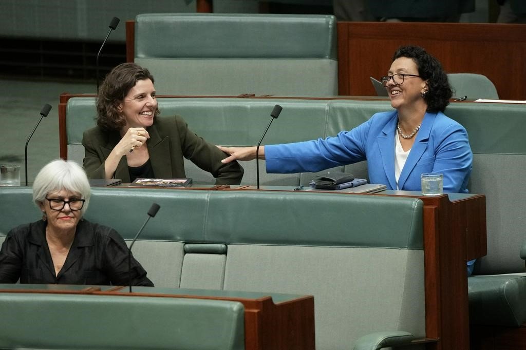 Two woman laugh as they sit side-by-side in the House of Representatives.