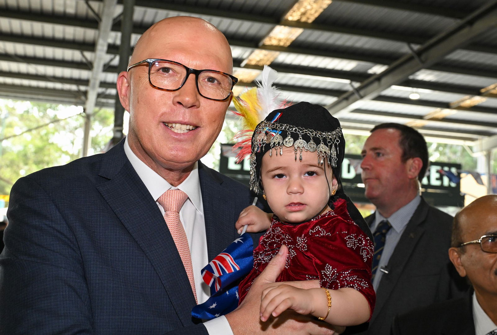 Peter Dutton smiles while holding an unimpressed-looking child.
