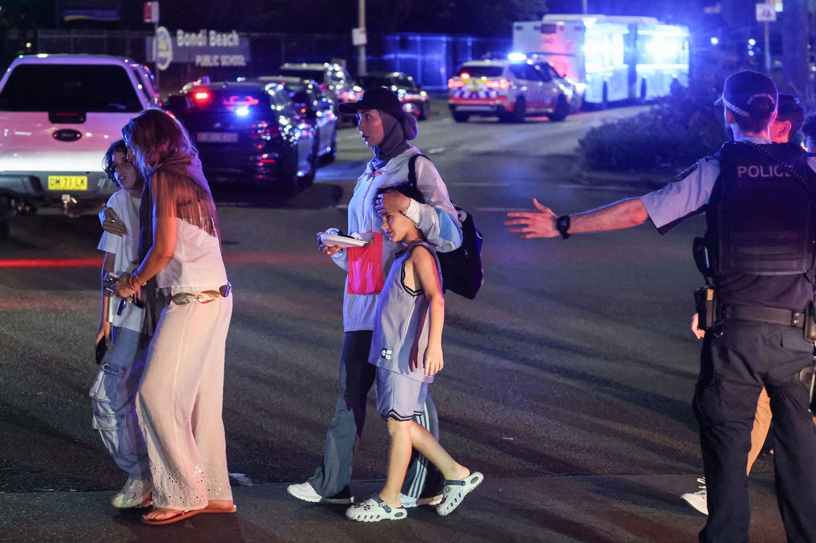 A woman walks a child across a street ushered by police in the aftermath of the Bondi shooting incident