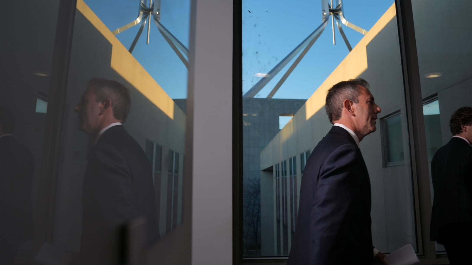 Jim Chalmers walks past a glass window.