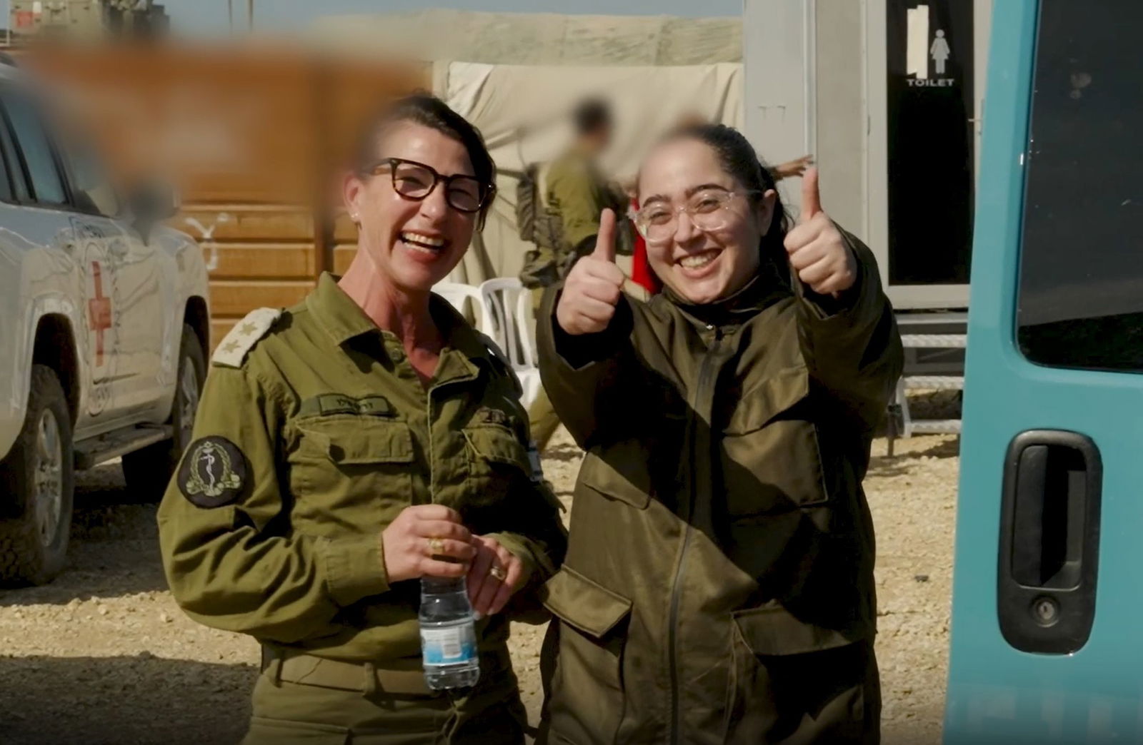 A woman gives the thumbs up to the camer while another woman smiles