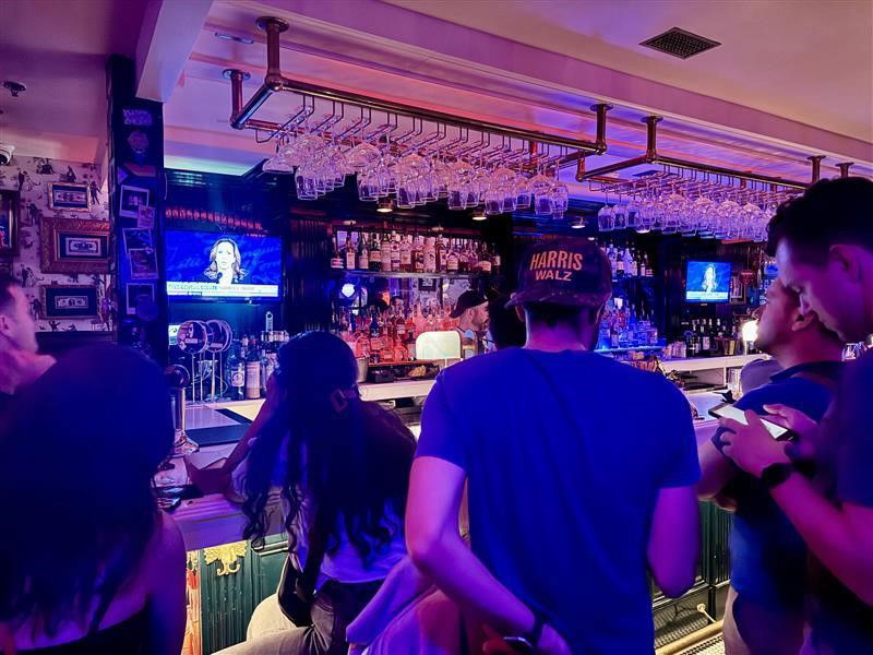 People stand at a pub bar where the presidential debate is being broadcast on screens