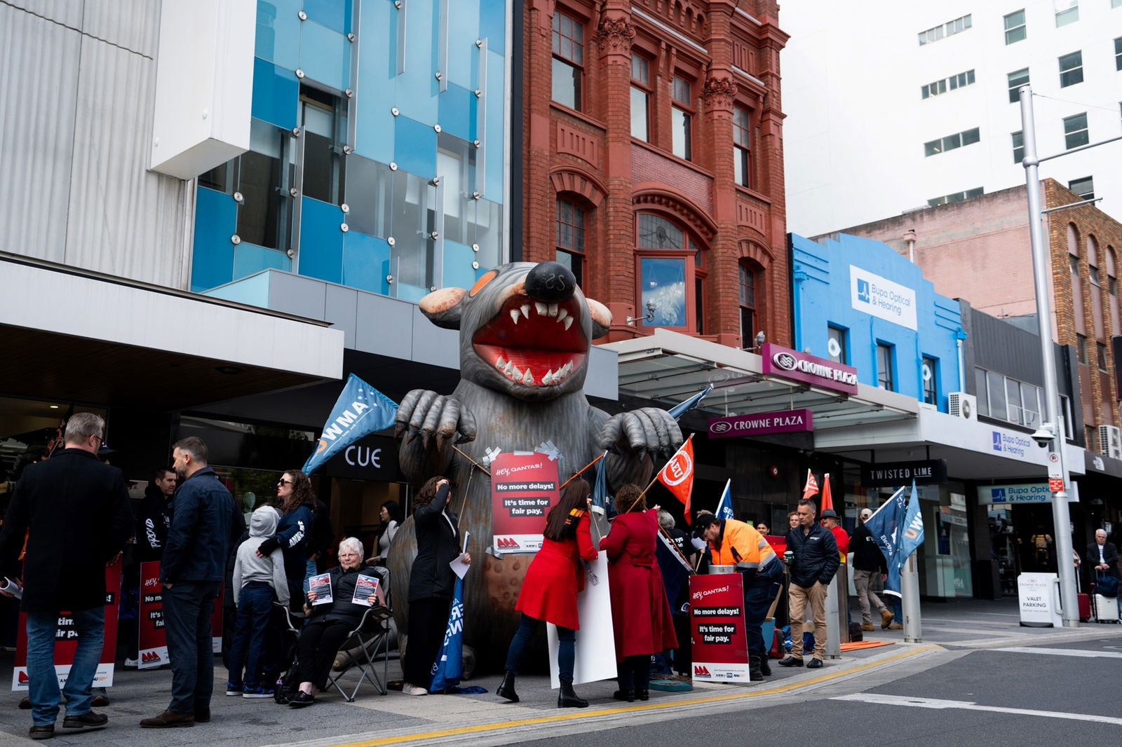 Workers holding union flags and signs around a large blow-up rat on a street in the Hobart CBD.