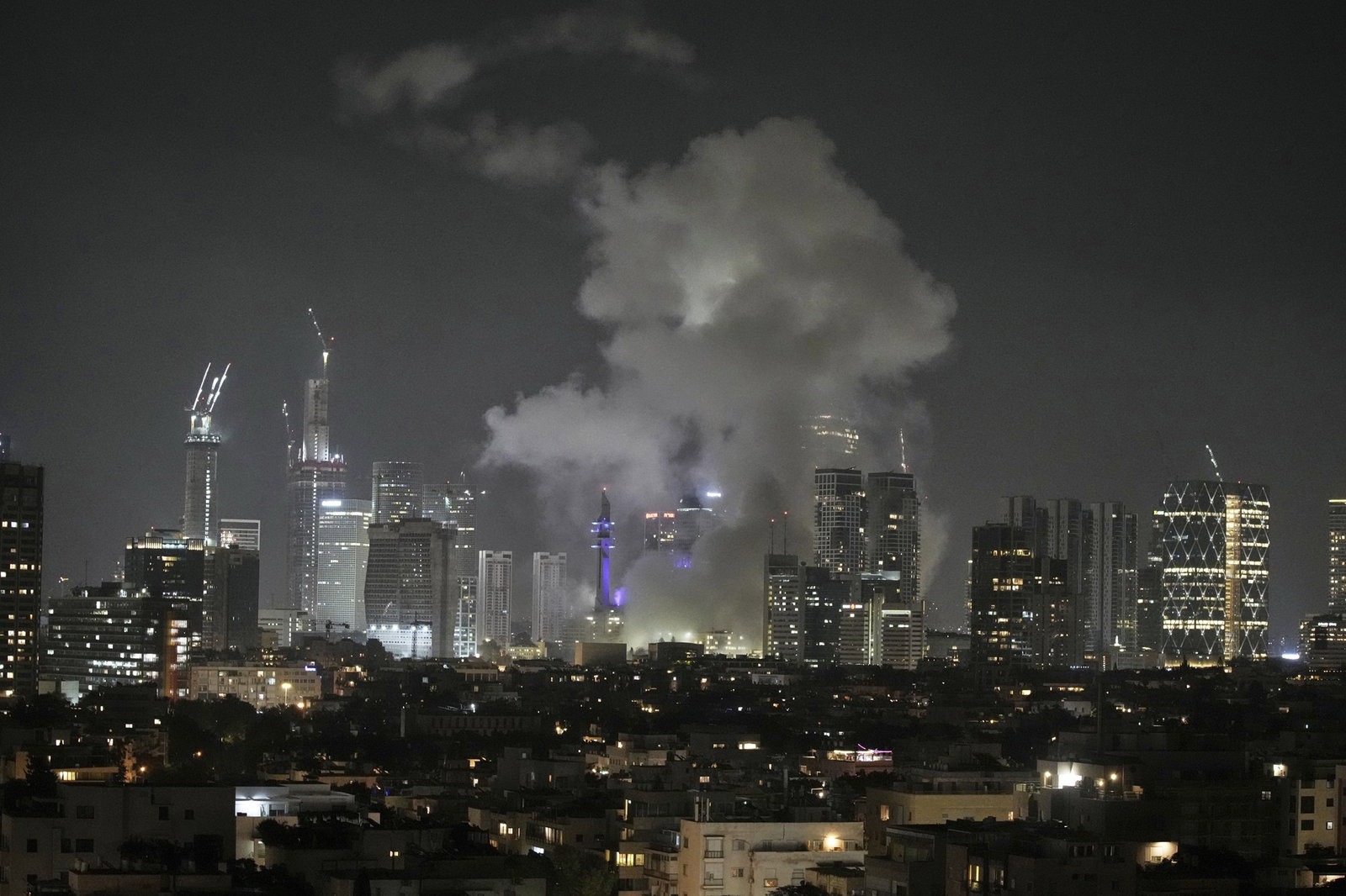 Smoke rises at night between a skyline of the city full of tall buildings