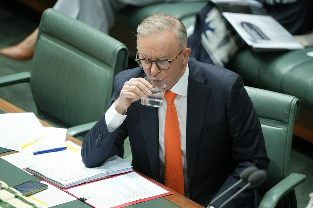 A middle-aged man in a suit sips water while sitting in parliament.