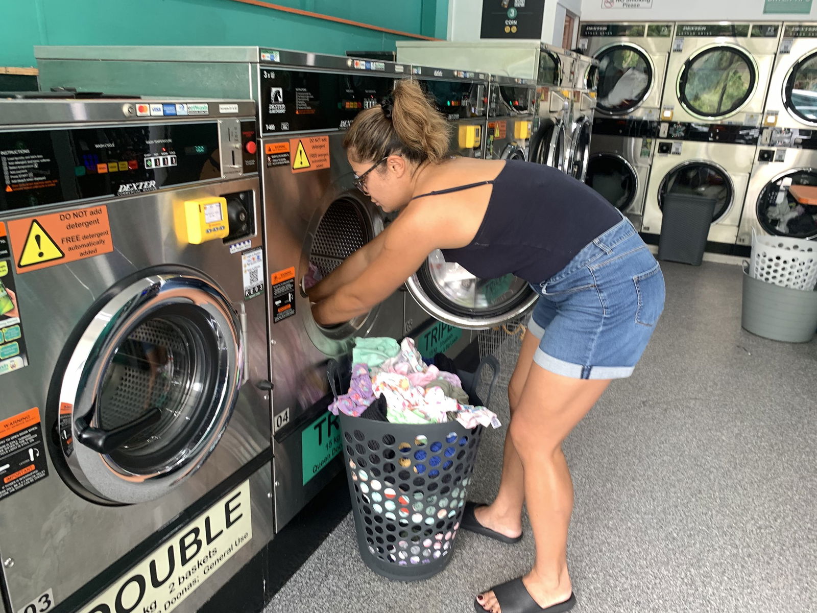 A woman filling up a silver washing machine with clothes. 