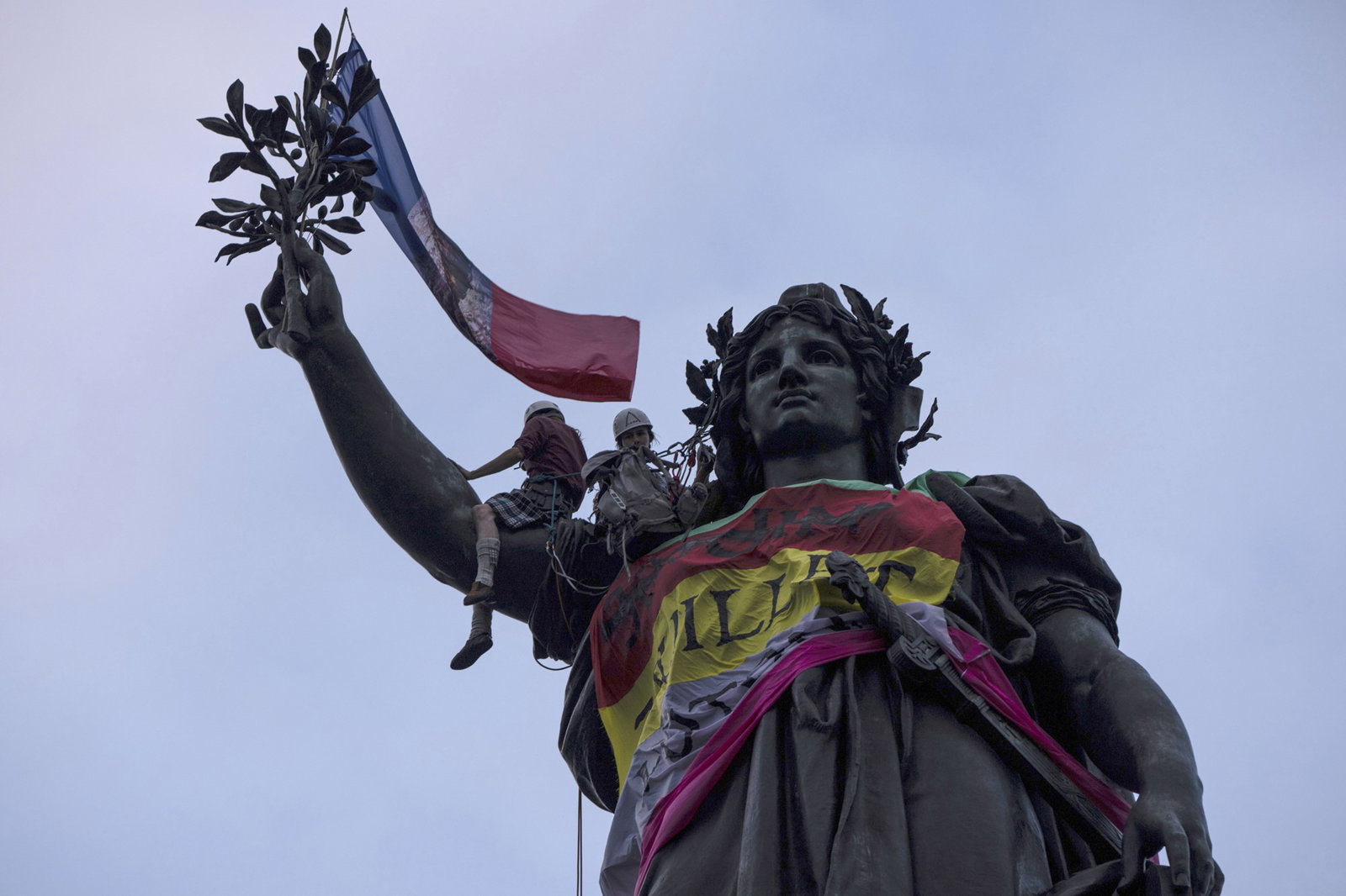 A statue covered in a french flag with people climbing 