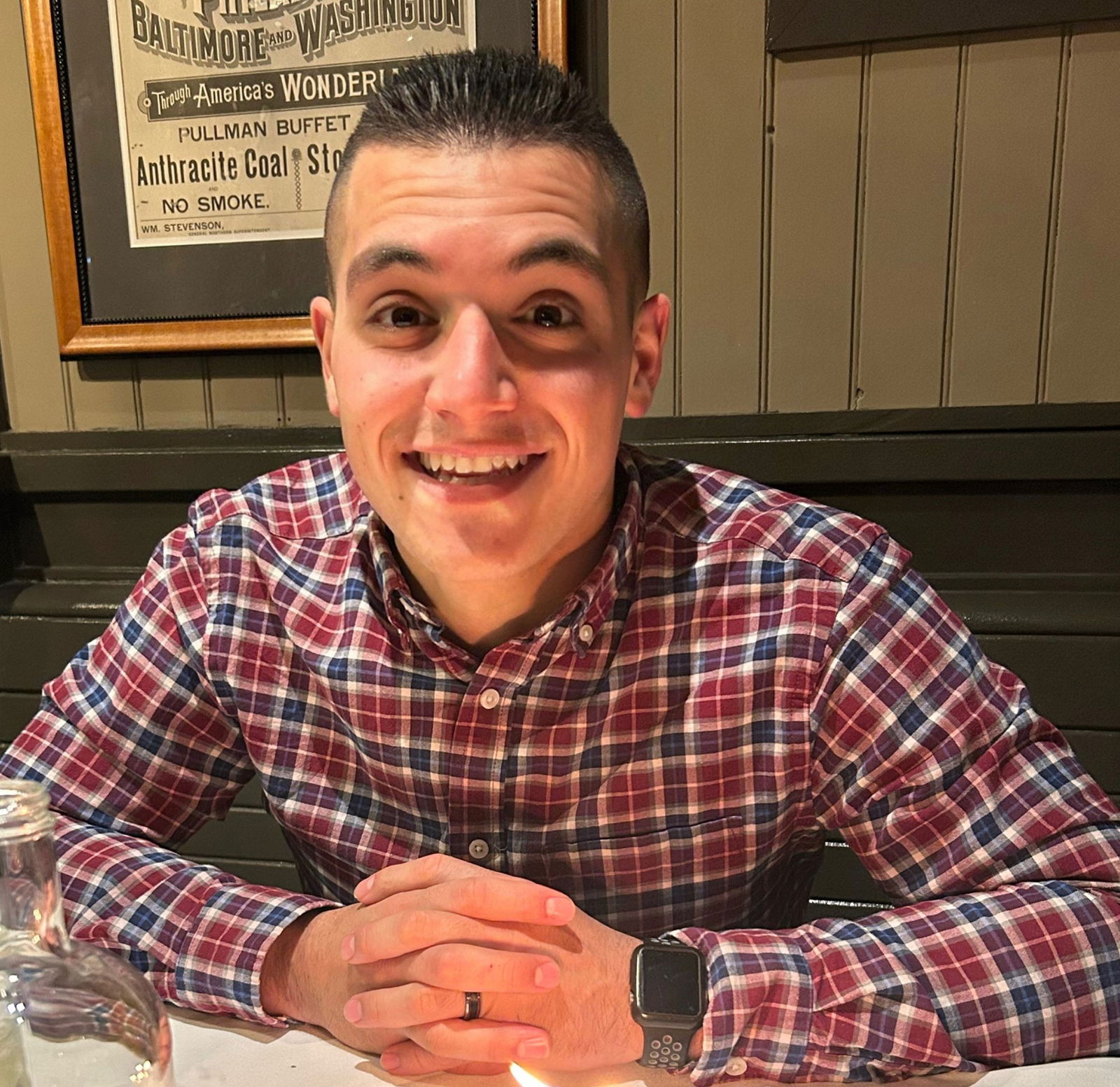 A man in a checkered shirt smiles at a table.