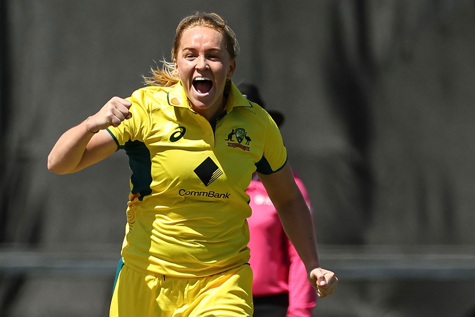 A woman in a yellow Australia cricket top pumps her fists and smiles