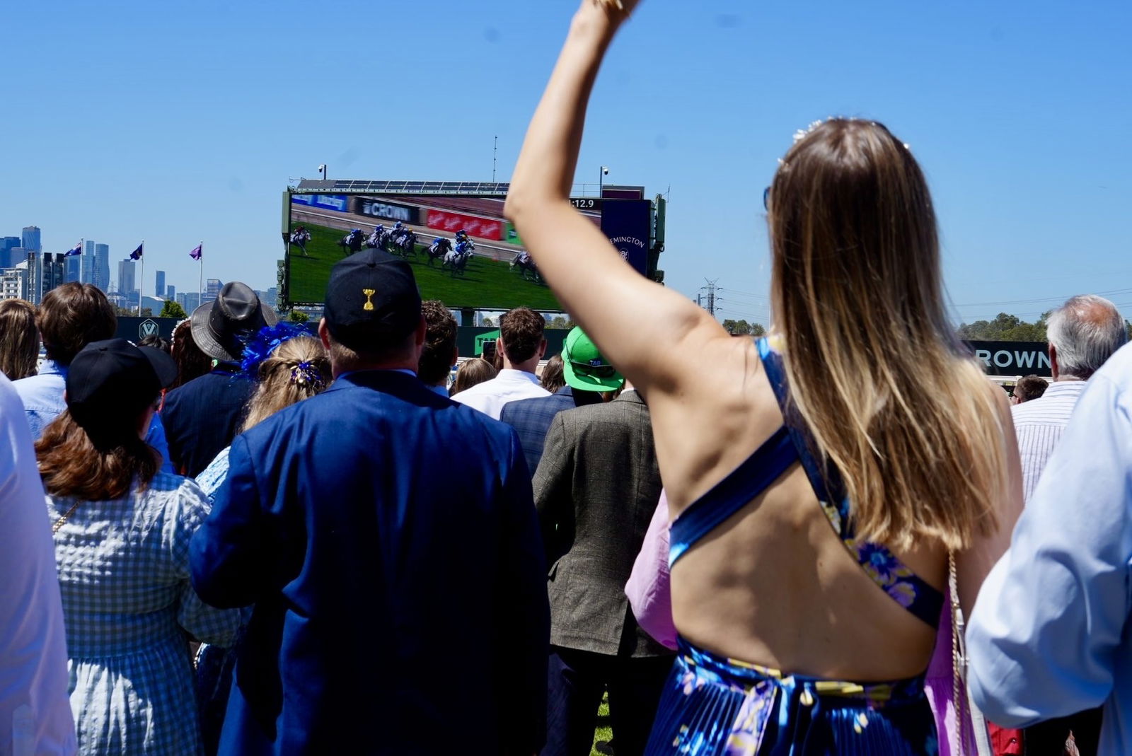 A lady fist pumps into the air while watching a horse race on a screen.