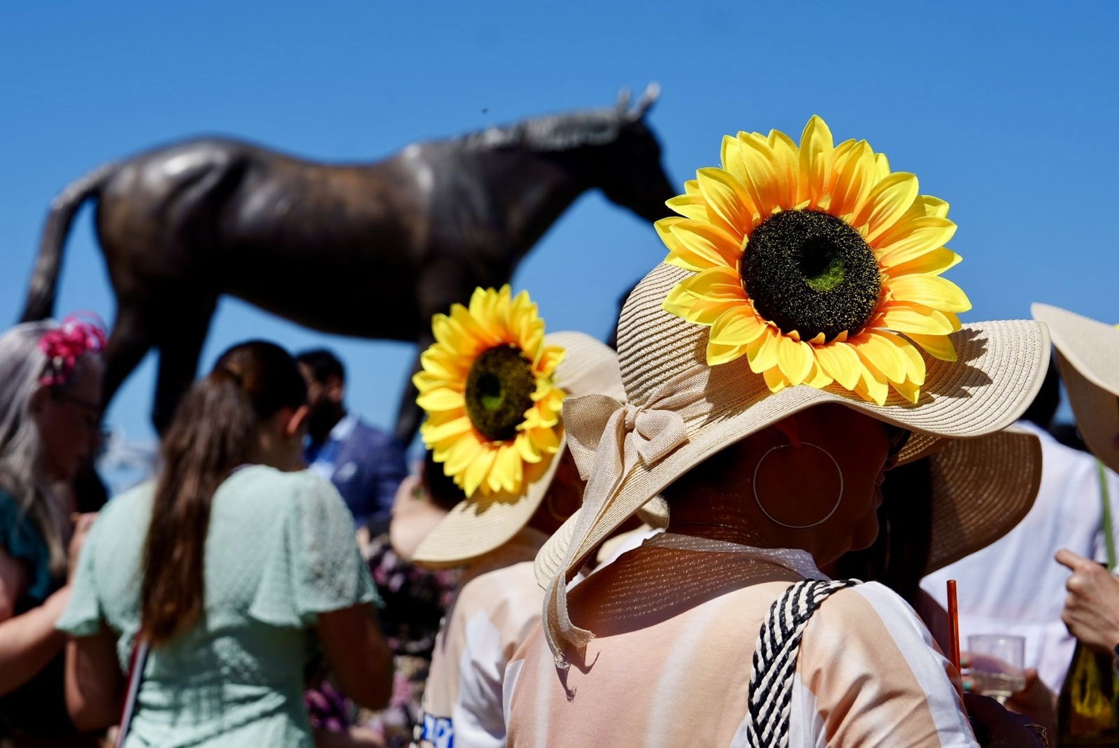 A woman wears a big sunflower on her hat.