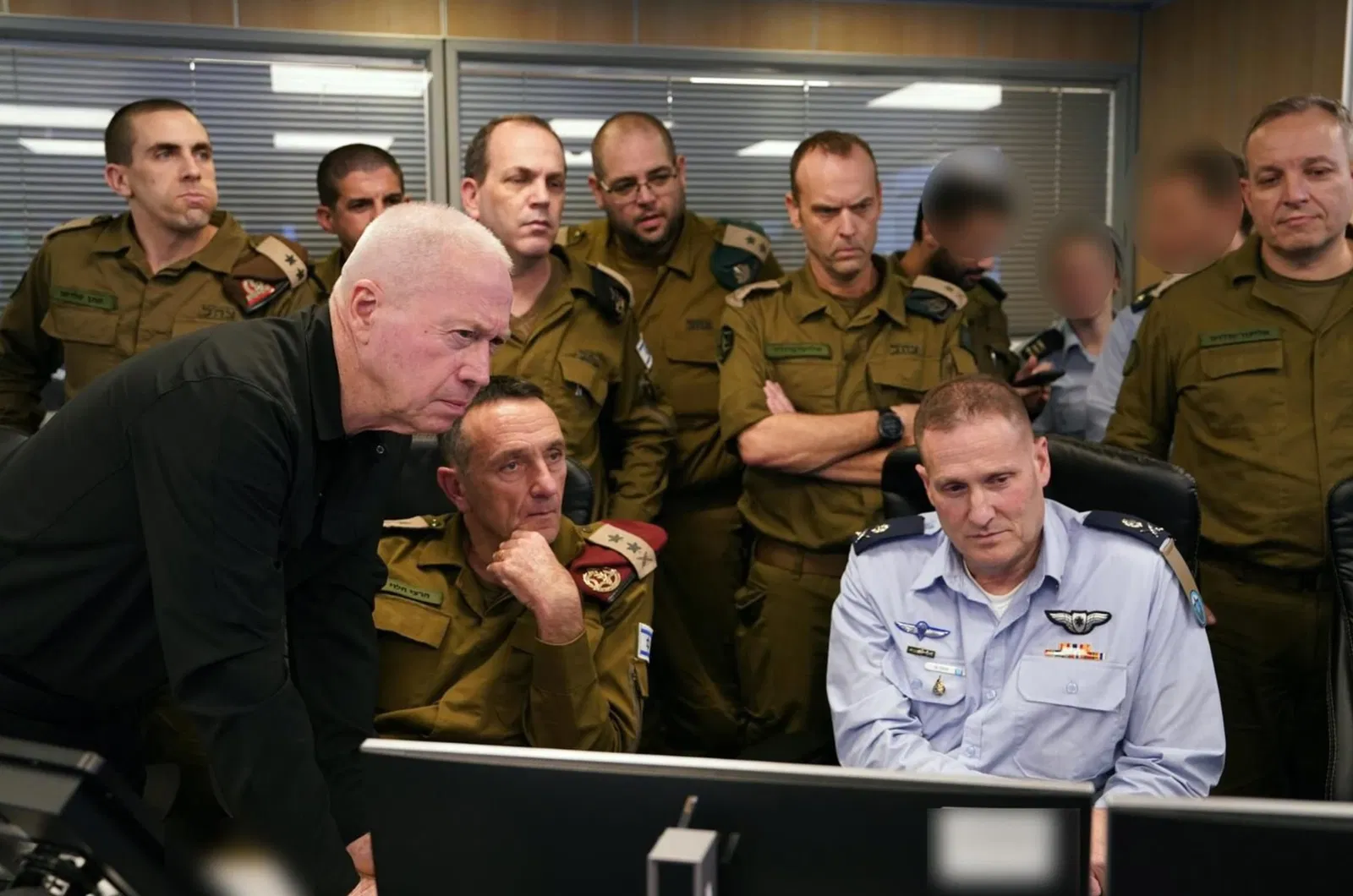 A large number of men crowd around a computer.