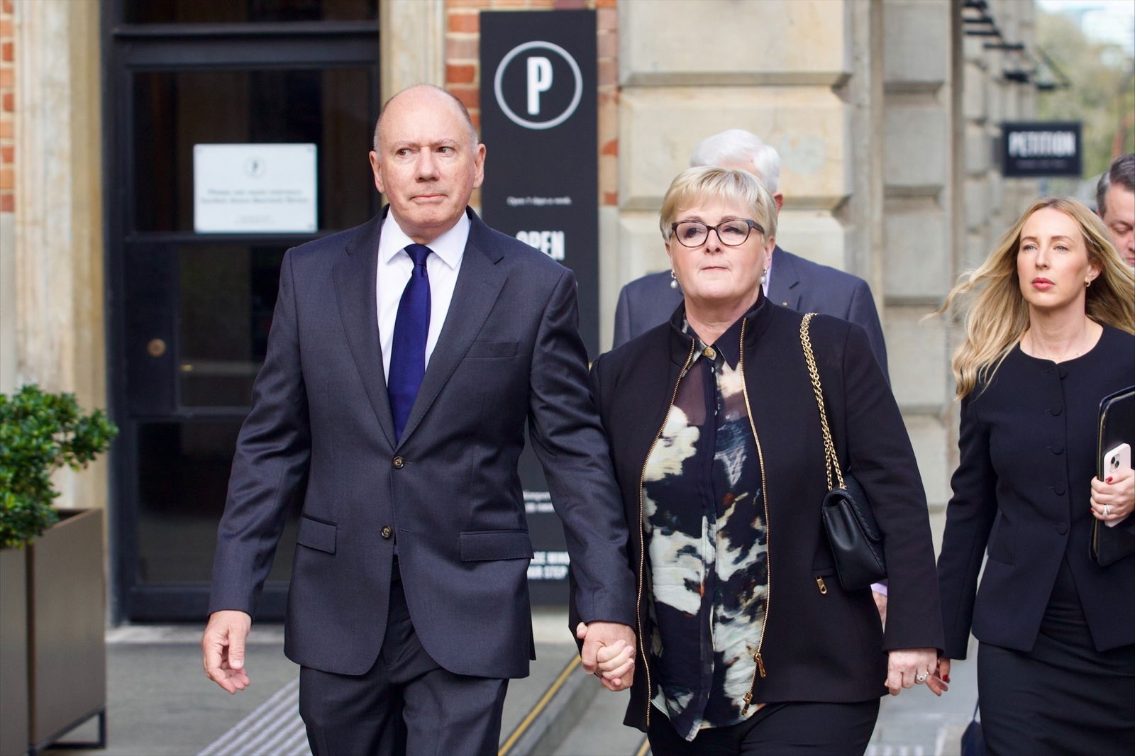 Linda Reynolds in a dark outfit holds hands with Robert Reid, in a suit.