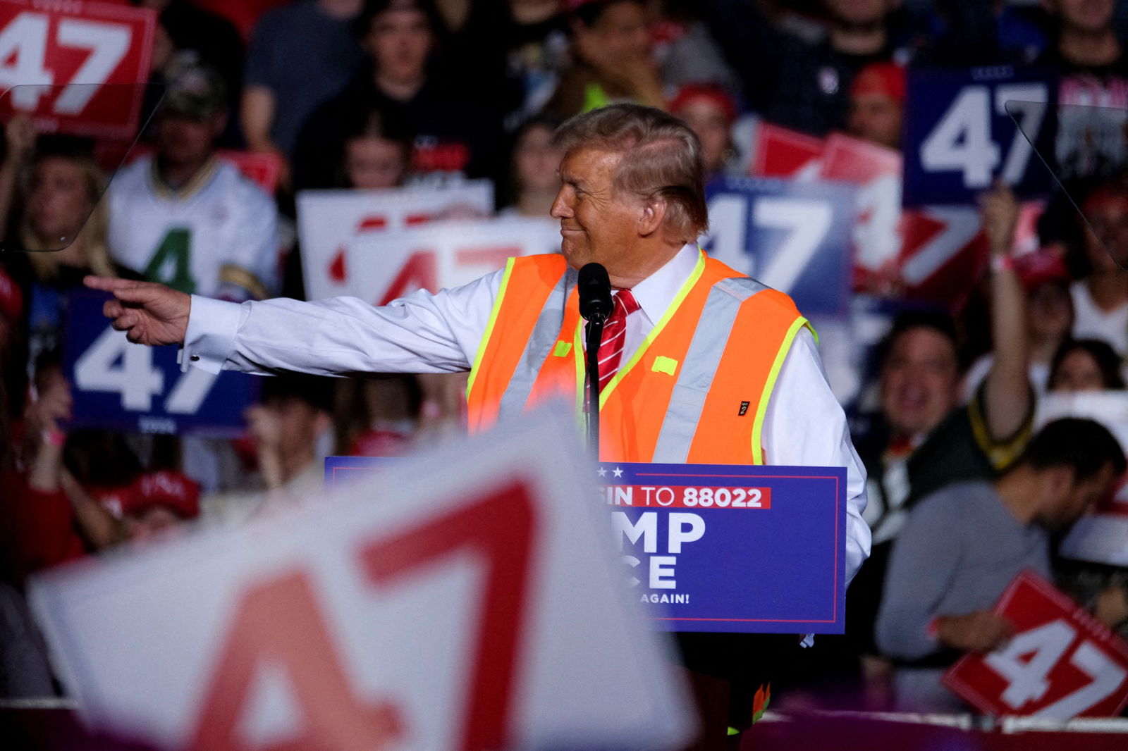 Trump, wearing a hi-vis vest, points to spectators during a rally