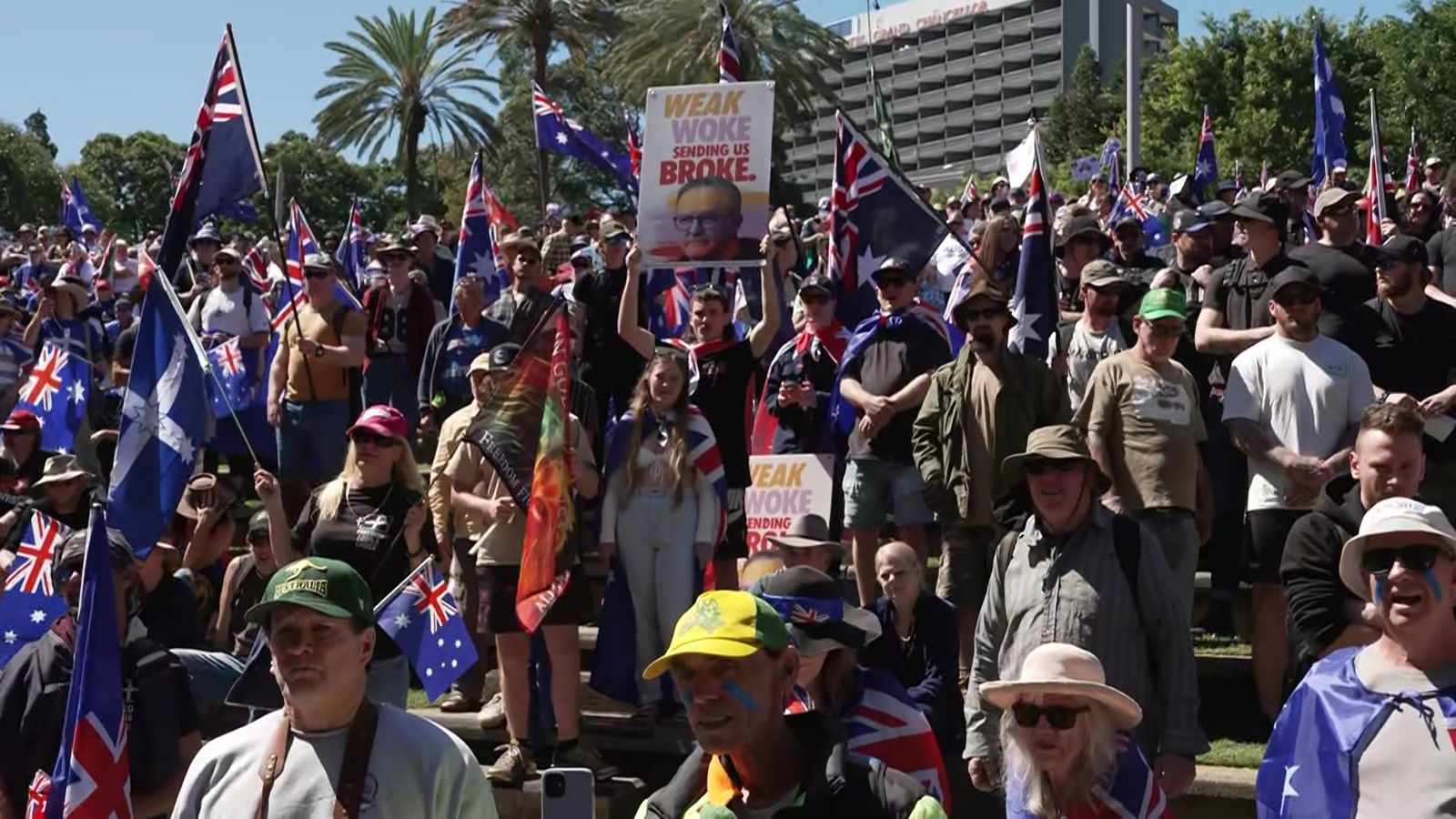 Personas que sostienen letreros y banderas australianas