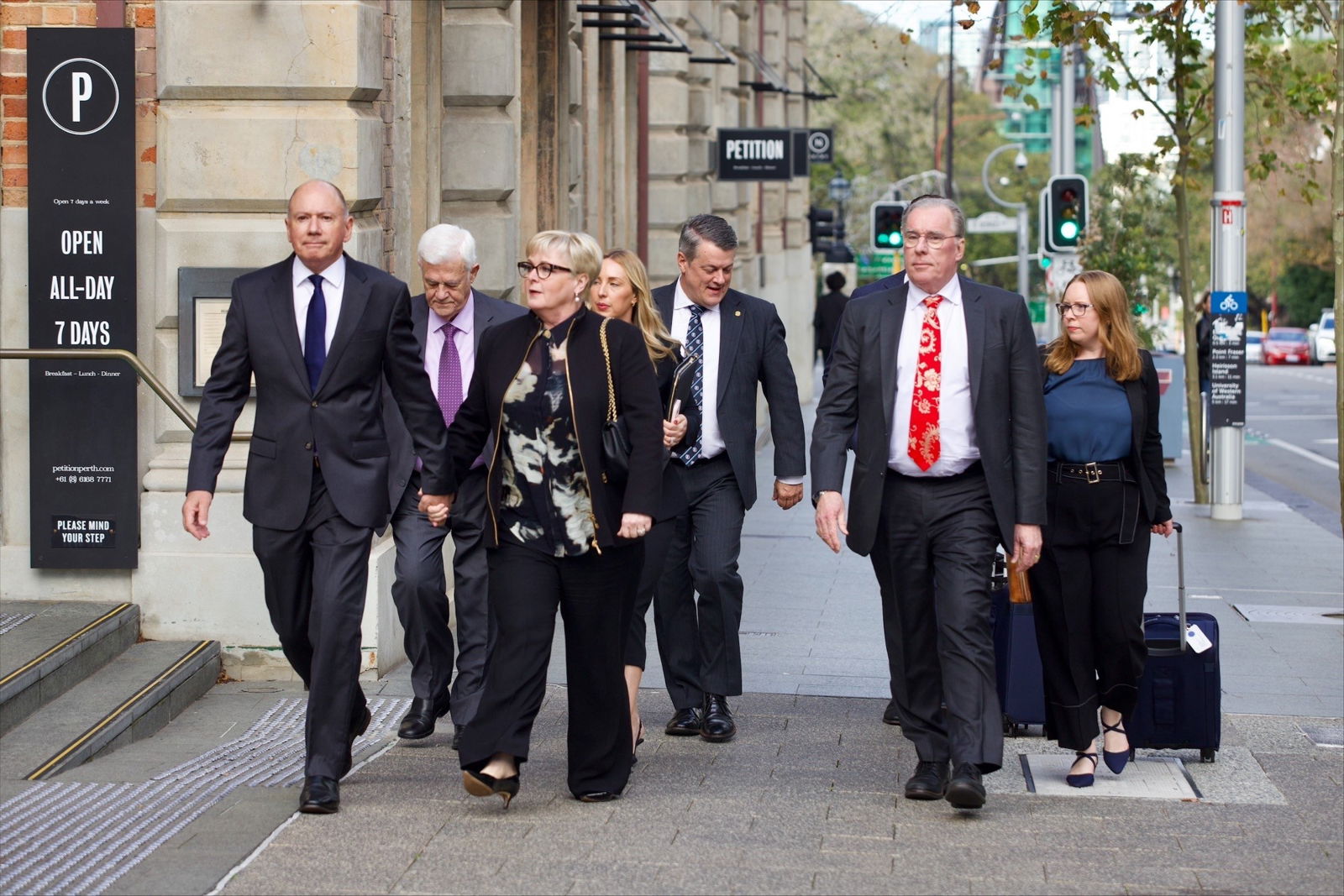 A group of people in suits walks down a CBD footpath