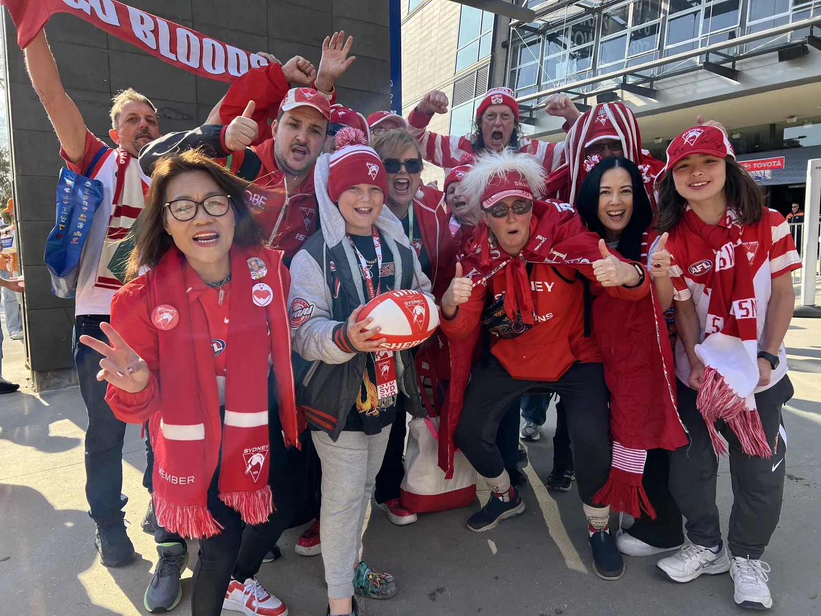 A group of adults and children smiling, dressed in red and white Sydney Swans gear.