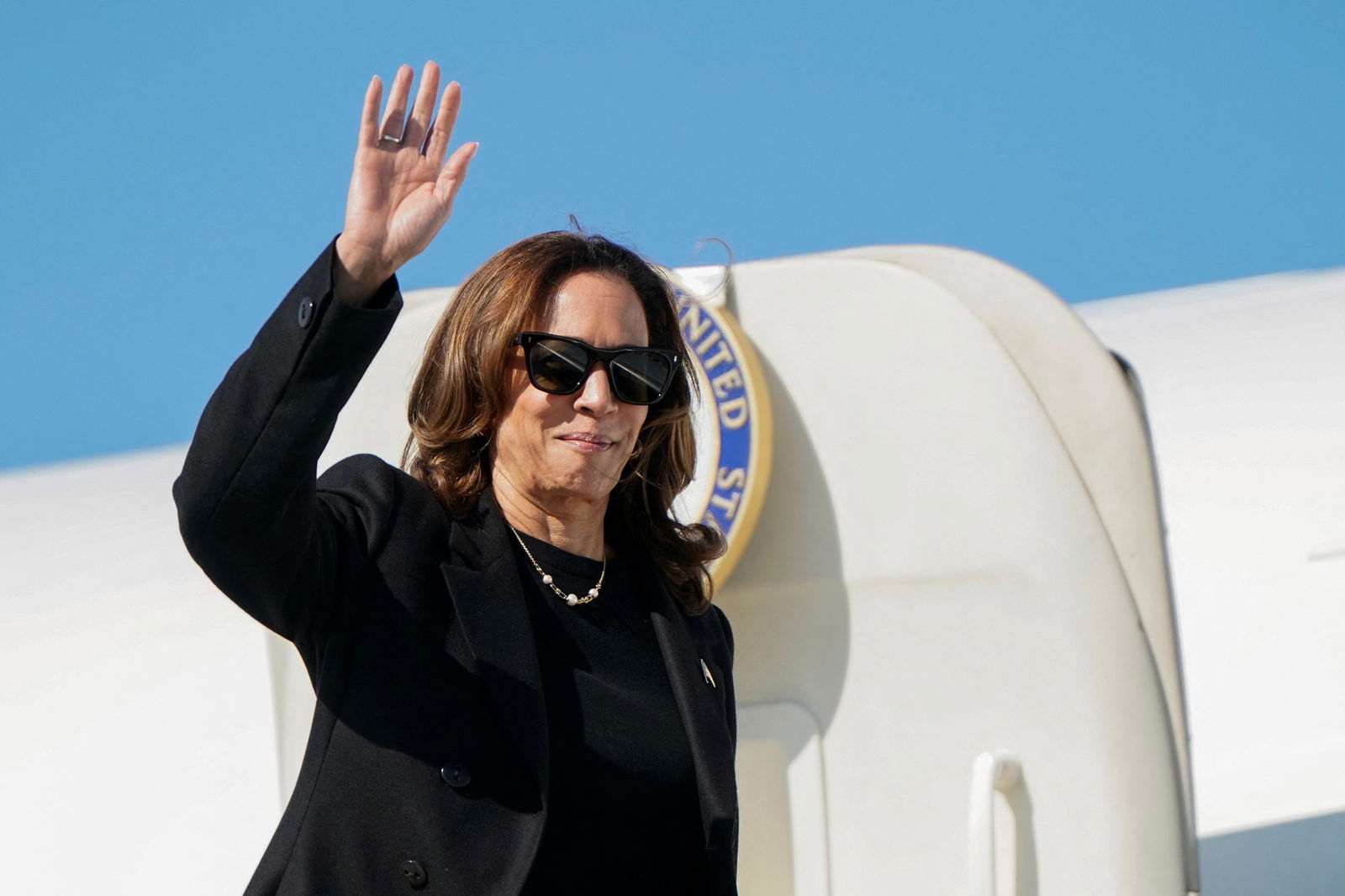 Kamala Harris steps off a plane wearing sunglasses and waves