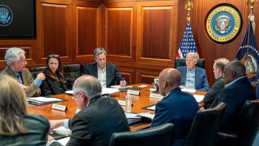 Joe Biden sits in a board room with eight other people.