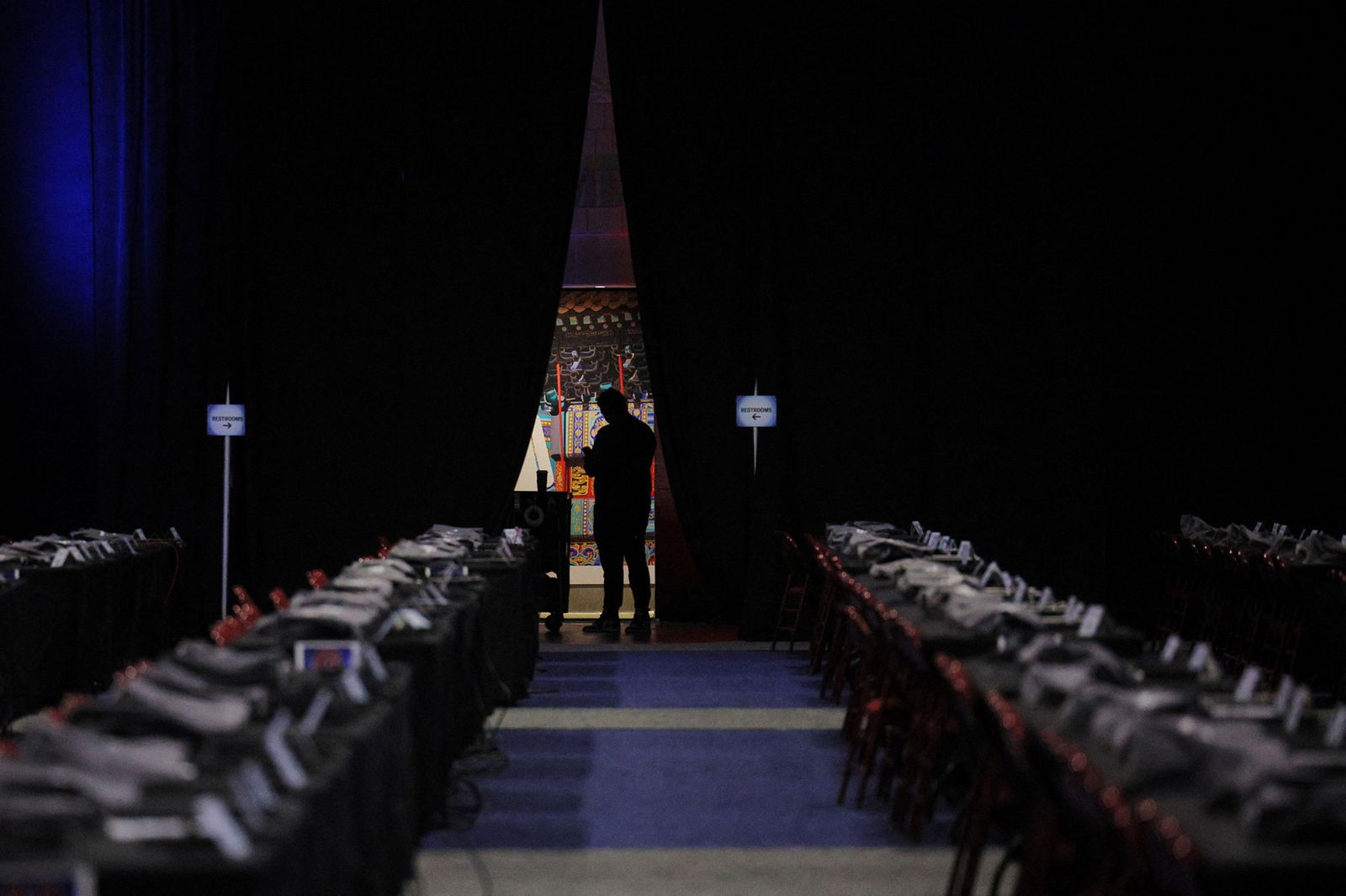 People stand at the end of rows of chairs, their silhouettes outlined in a door frame