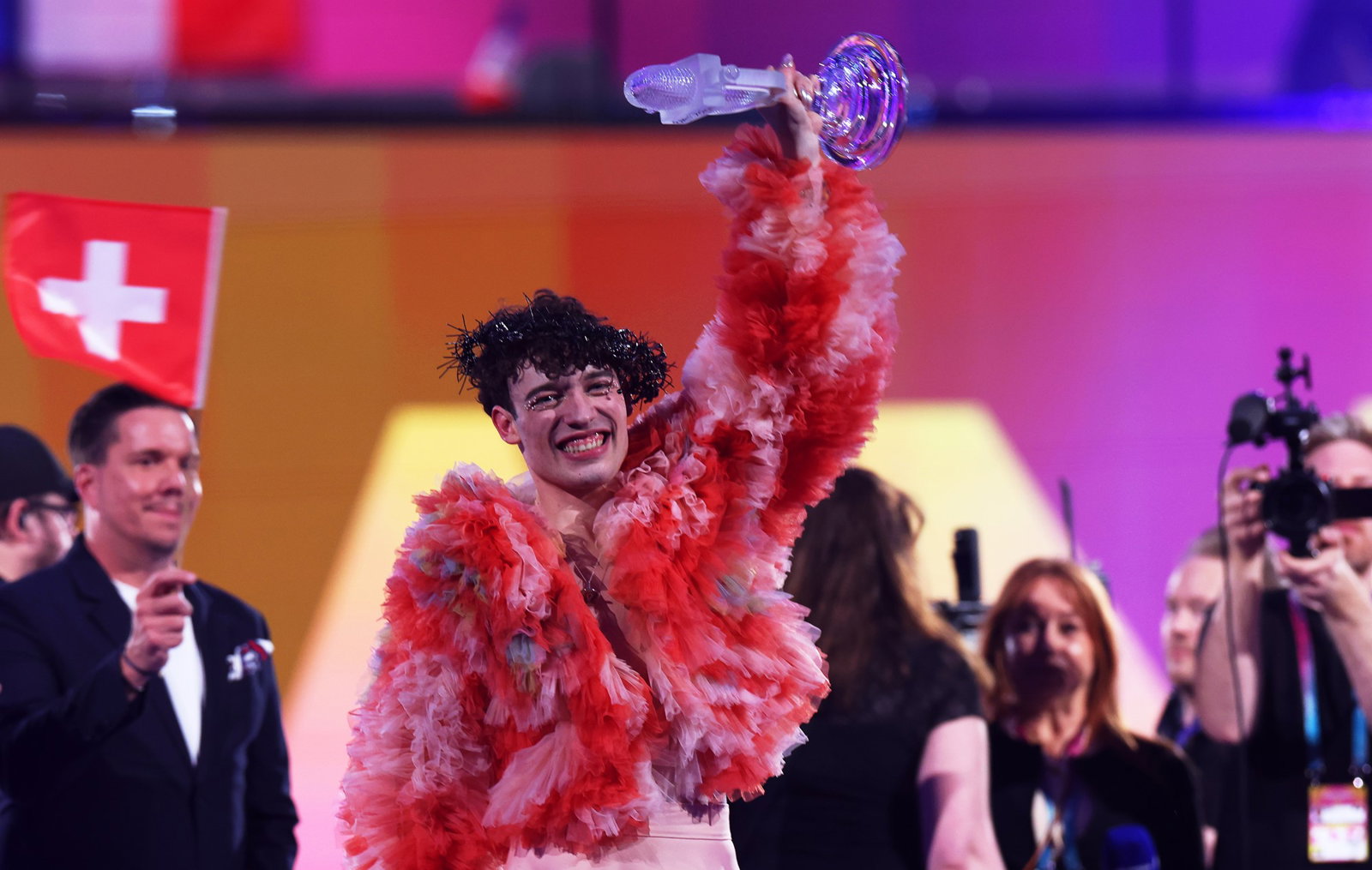 Artist Nemo in red with the eurovision trophy in his hand up on stage
