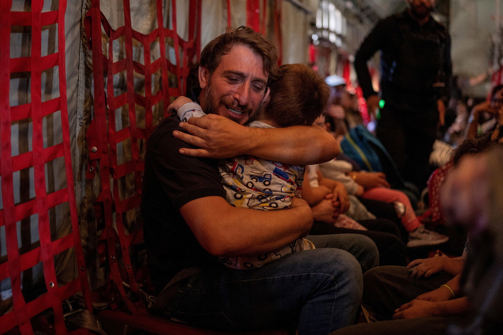 a man in the belly of a cargo plane holds his small son tightly while crying
