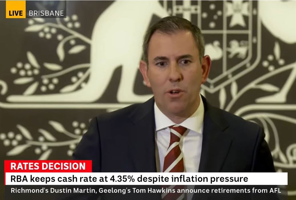 A man wearing a suit and tie speaks in front of the Australian emblem.