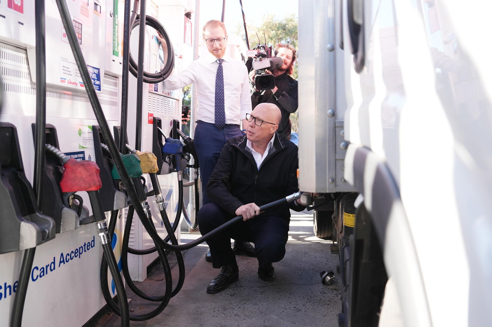 Peter Dutton crouching alongside a truck as he fills the vehicle up with a petrol bowser pump.