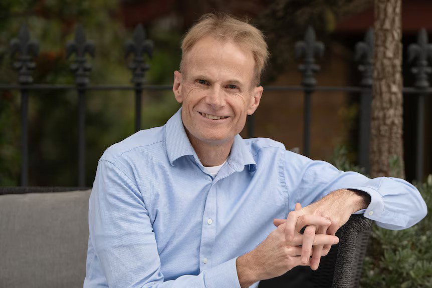 Richard Scolyer in a blue shirt, smiling as he sits.