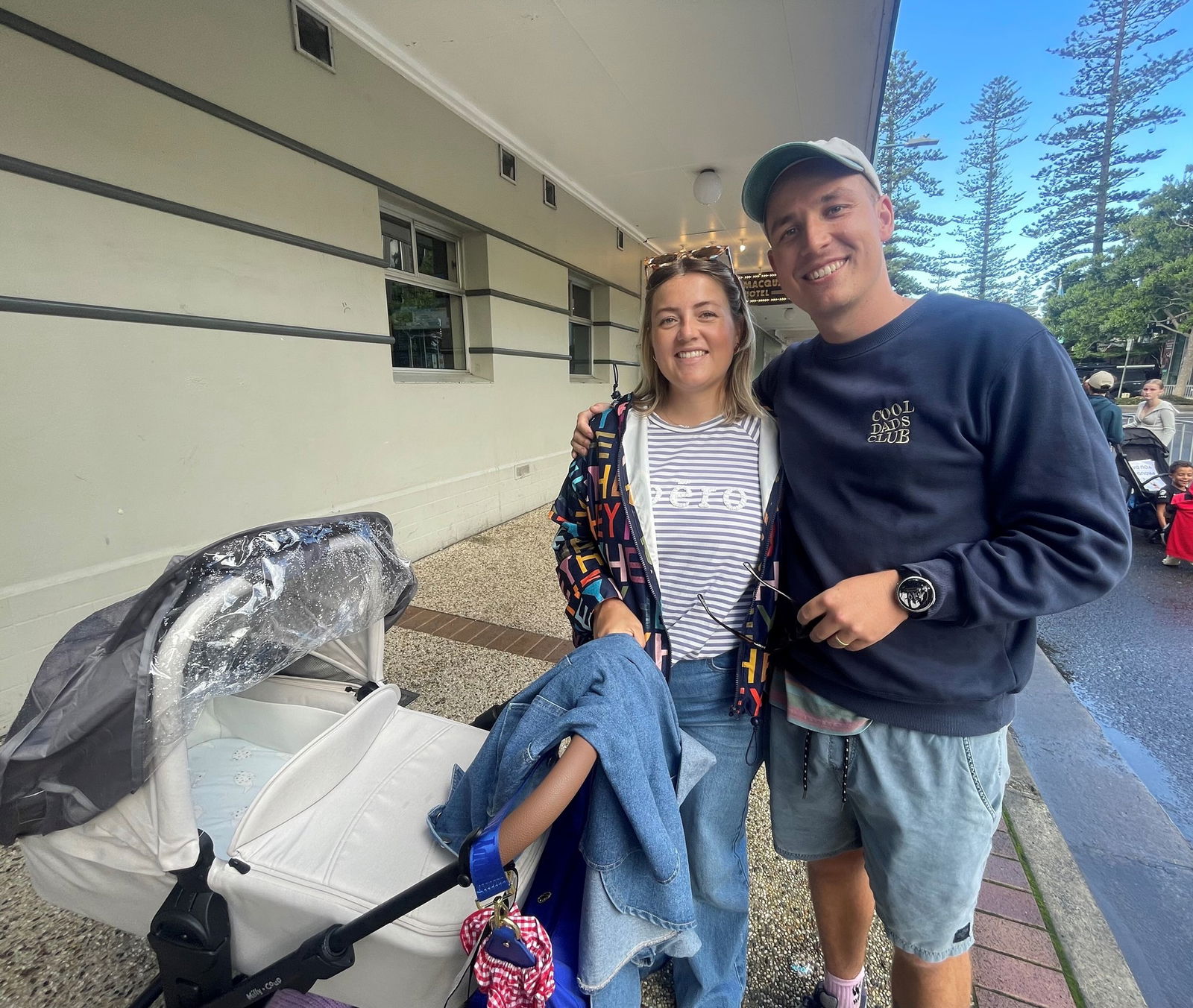 A woman in a striped shirt holds a stroller while a man in a cap hugs her