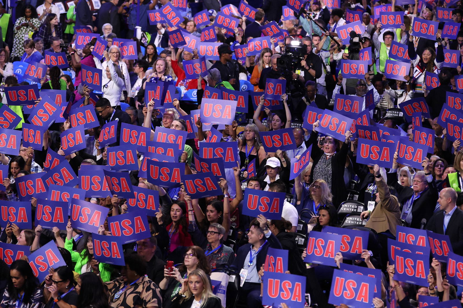 A crowd of people hold up blue and red signs that read 'USA'