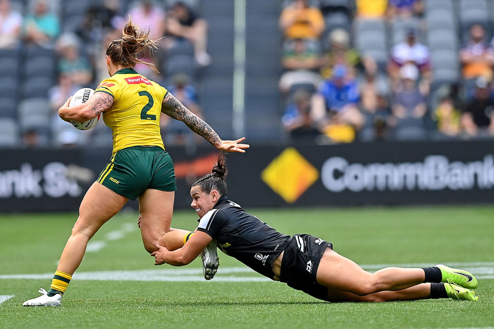 Julia Robinson runs with the ball for Australia. Shanice Parker of New Zealand tries to tackle her by the legs.