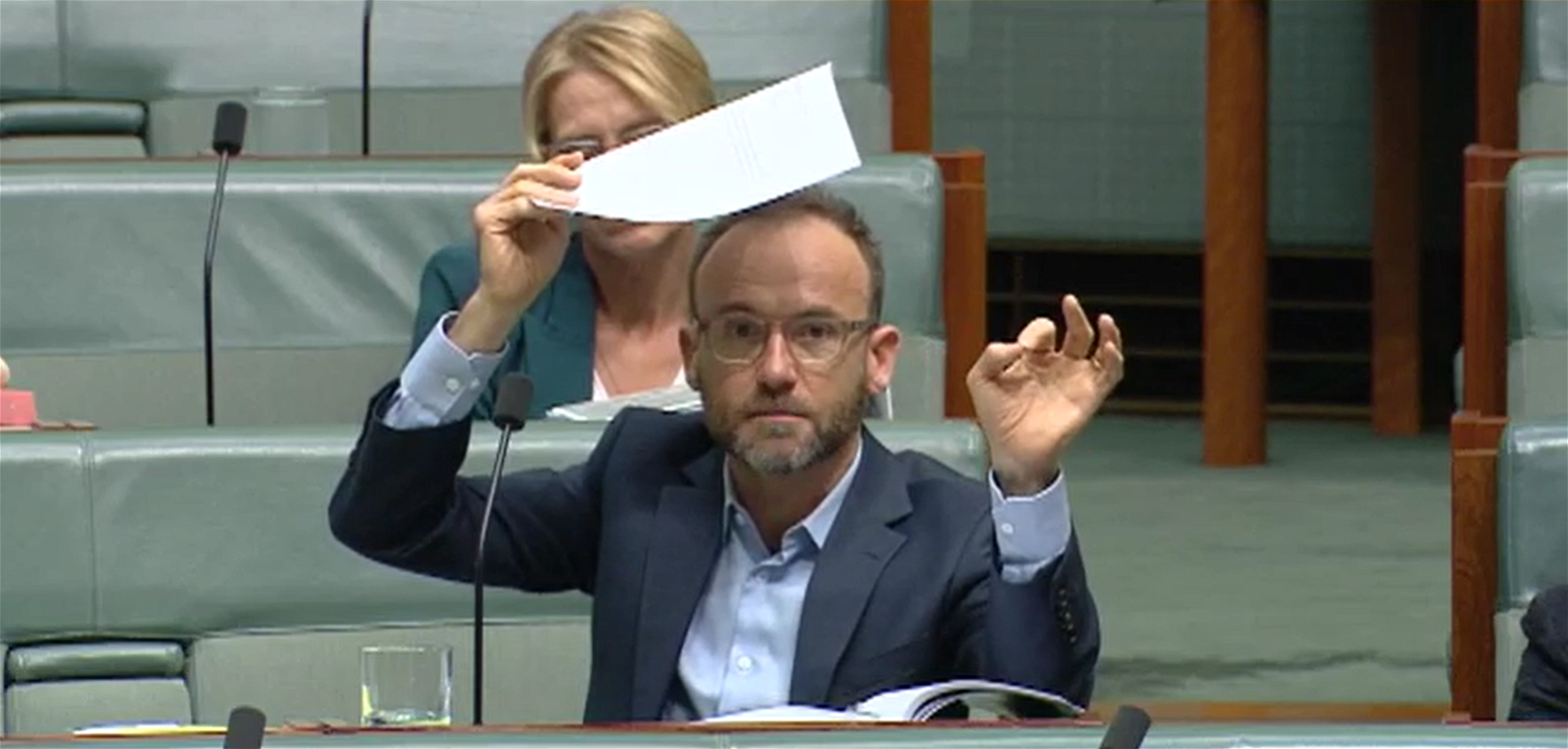 Adam Bandt holds a piece of paper over his head.