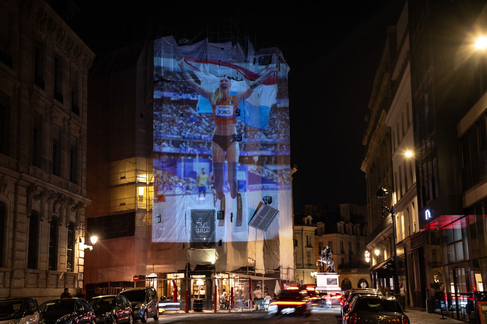 A photograph of Fleur Jong of Team Netherlands celebrating after winning a gold medal in the Women's Para Athletics 100m T64 Final is projected onto a building in Paris.