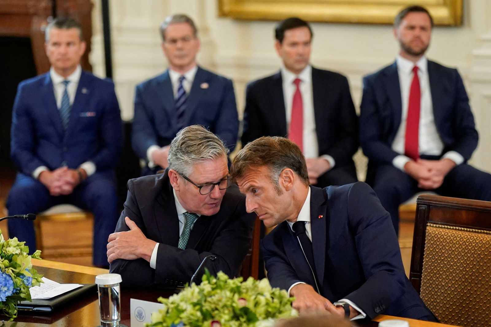 Emmanuel Macron leans toward Keir Starmer as the two have an aside at the meeting table