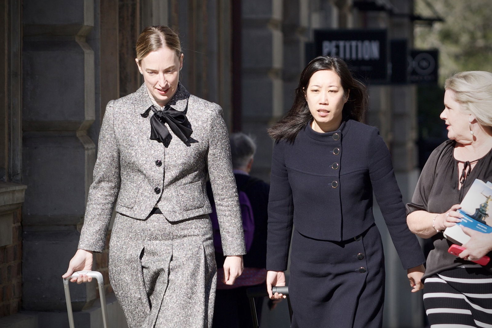 Two smartly dressed women walk on a city street. 