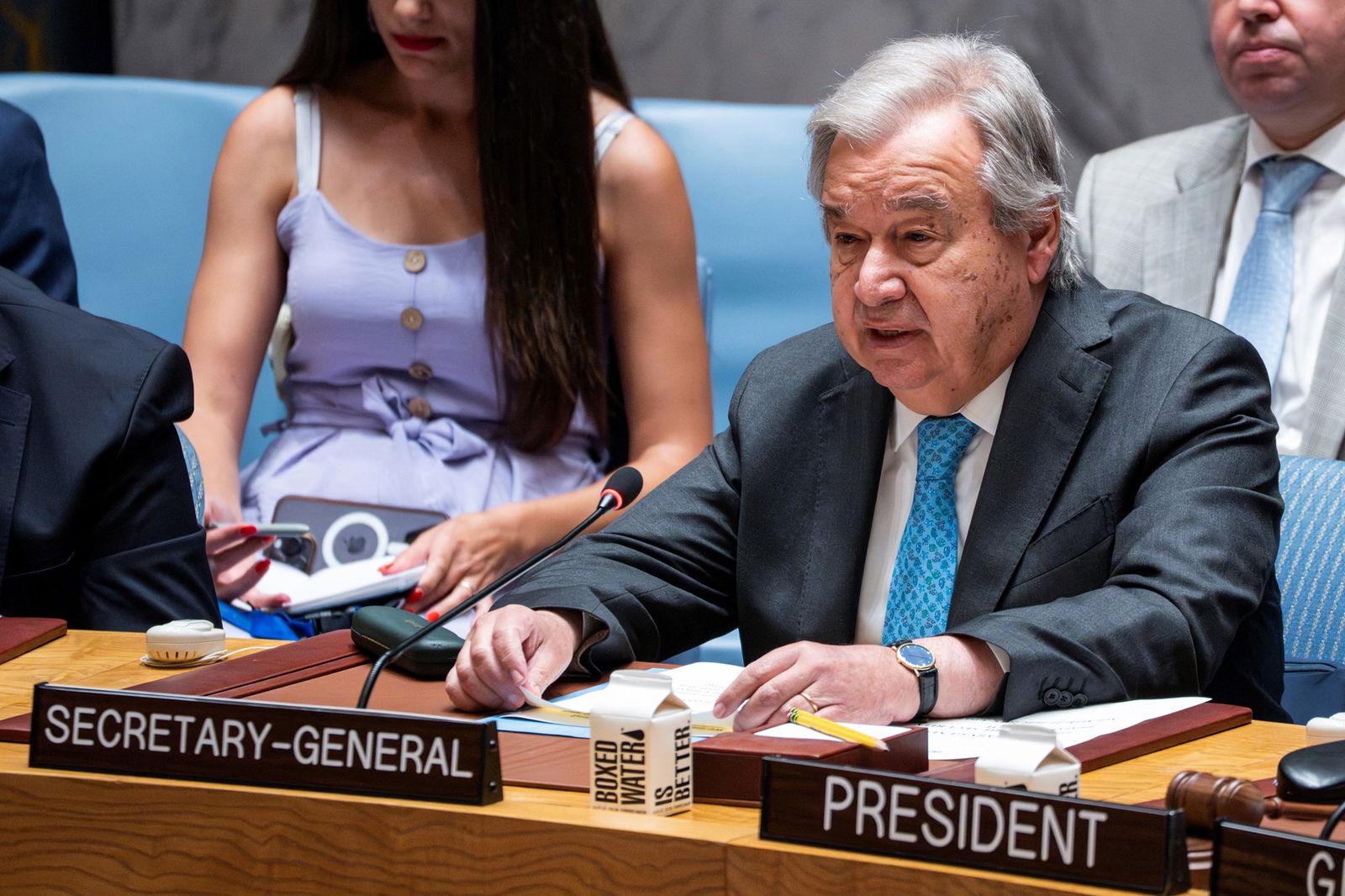 An elderly man sits at a desk with the placard'Secretary-General' in front of him