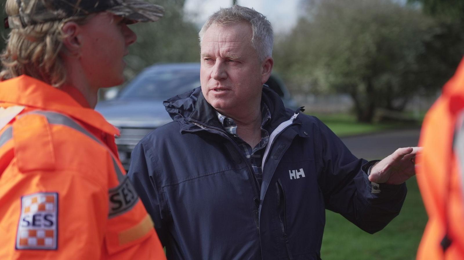 Premier Rockliff speaks as SES workers in orange jackets walk by